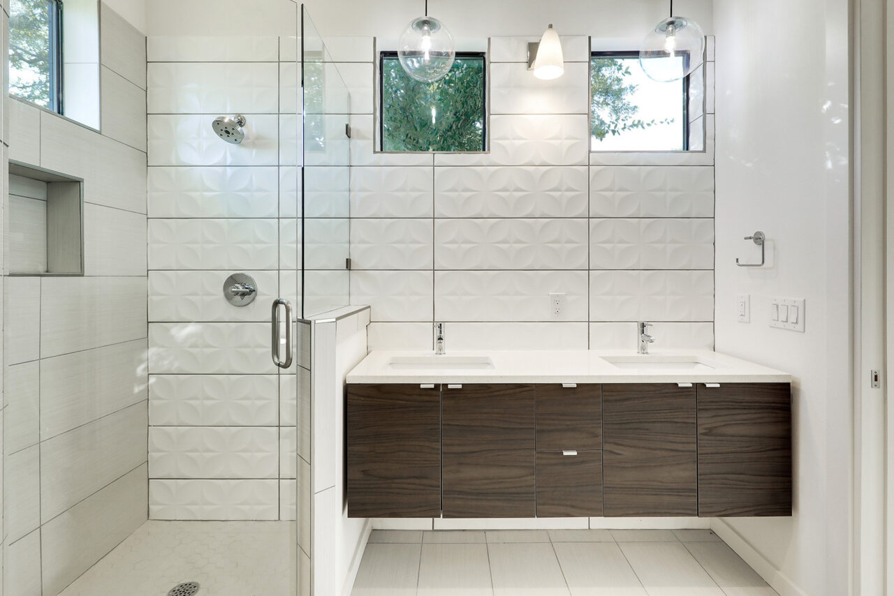 Dark wood bathroom vanity beside a glass-enclosed shower with white tile