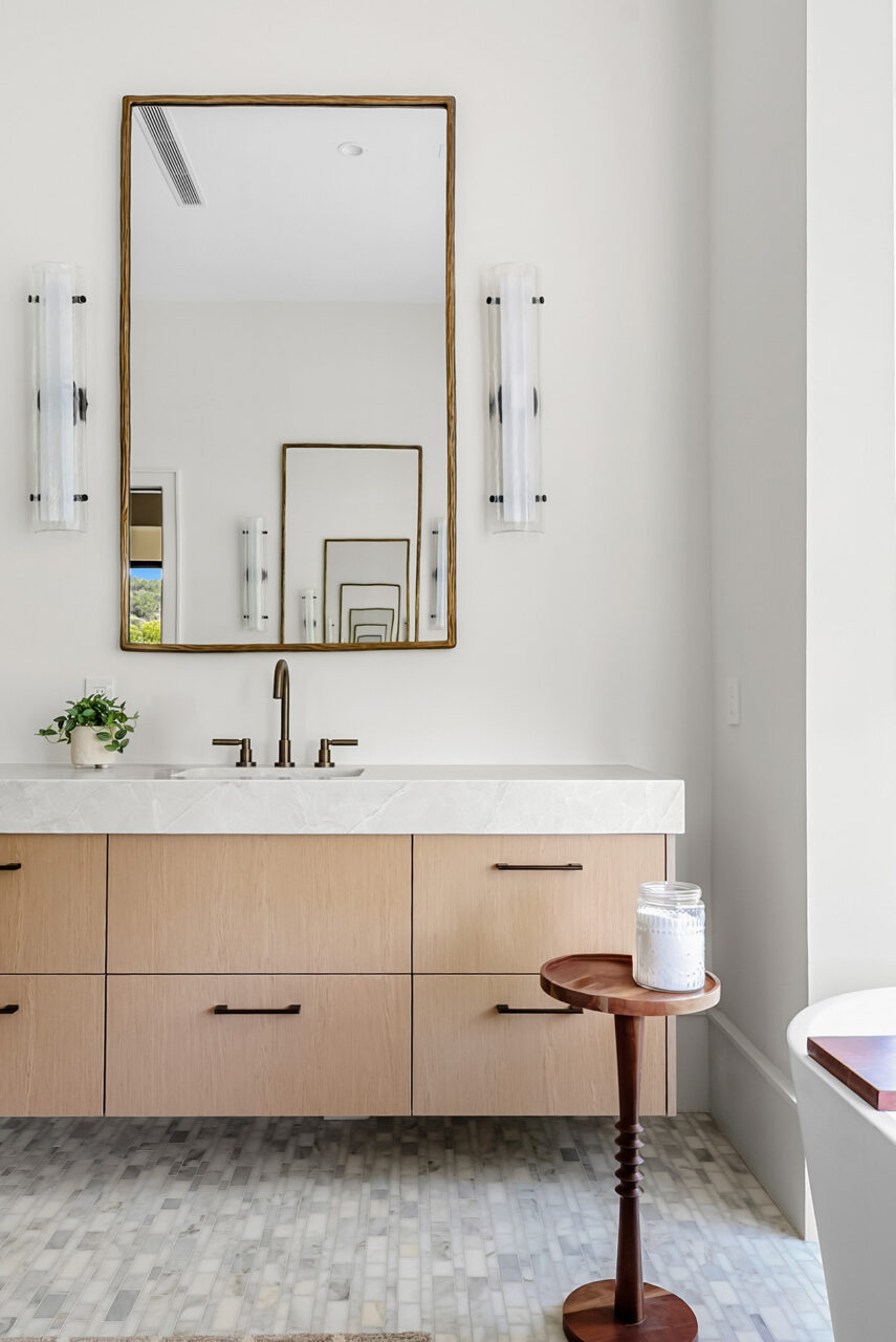 Light wood bathroom vanity beneath a tall framed mirror and wall sconces