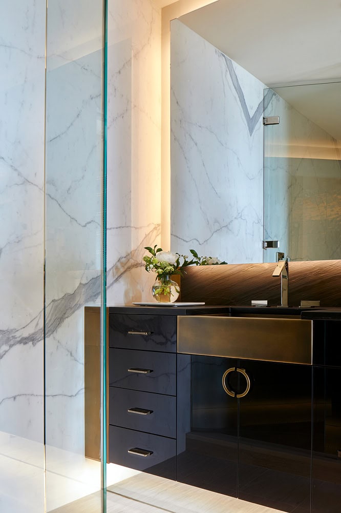 Dark bathroom vanity with backlit mirror and glass shower panel
